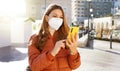 Woman in puffer jacket and medical face mask using her mobile phone outdoors