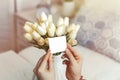 Woman pulling blank greeting card from bouquet of white tulips flowers. Copy space. Mock up. Sinlight. Royalty Free Stock Photo