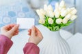 Woman pulling blank greeting card from bouquet of white tulips flowers. Mother day, Copy space. Mock up. Royalty Free Stock Photo