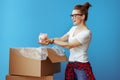 Woman pulls out pig piggybank out of cardboard box on blue Royalty Free Stock Photo