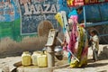 Woman pumps water to plastic containers with a hand pump at the street in Orchha, India.