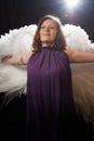 Woman in purple dress and white wings posing in studio on a black background. Photo shoot with model looking as angel Royalty Free Stock Photo