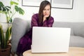 Woman in purple nightwear on sofa couch using laptop computer in dark evening at home