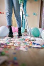 Woman with pushbroom cleaning mess of floor in room after party confetti