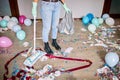 Woman with pushbroom cleaning mess of floor in room after party confetti