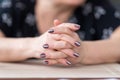 A woman sits at a table, her fingers intertwined. Fingers clasped, hands resting on the table Royalty Free Stock Photo