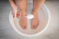 Woman put spoon of baking soda in bath with hot water for his feet. Homemade bath soak for dry feet skin. Royalty Free Stock Photo