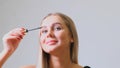 Woman puts black mascara on her eyelashes with makeup, photo of attractive blonde on a white and gray background. Royalty Free Stock Photo