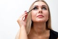 Woman puts black mascara on her eyelashes with makeup, photo of attractive blonde on a white and gray background. Royalty Free Stock Photo