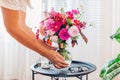 Woman puts bouquet of pink flowers in transparent vase on coffee table. Taking care of interior and summer decor at home Royalty Free Stock Photo