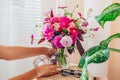 Woman puts bouquet of pink flowers in transparent vase on rattan table. Taking care of interior and summer decor at home Royalty Free Stock Photo