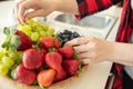 Woman puts green grapes, strawberries and blueberries