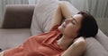 Woman puts hands behind head relaxing leaned on sofa