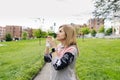 A woman puts on her face mask in a park with buildings in the background Royalty Free Stock Photo