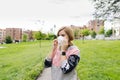 A woman puts on her face mask in a park with buildings in the background Royalty Free Stock Photo