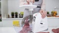 Woman puts pieces of raw meat into electric meat grinder. Electric mincer machine with fresh chopped meat. Preparation