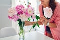 Woman puts peonies flowers in vase. Housewife taking care of coziness and decor on kitchen. Composing bouquet.