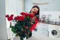 Woman puts roses in vase smelling flower. Housewife taking care of coziness on kitchen. Modern kitchen design Royalty Free Stock Photo