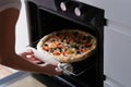 Woman puts pizza pan in oven closeup