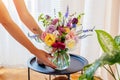 Woman puts transparent vase with bouquet of roses flowers on table. Taking care of interior and summer decor at home Royalty Free Stock Photo