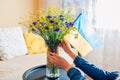 Woman puts Ukrainian flag in vase with bouquet of blue and yellow flowers at home. Symbol of freedom in Ukraine