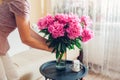 Woman puts vase with peonies flowers on table. Housewife taking care of coziness at home. Interior and spring decor