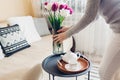 Woman puts vase with tulips flowers on table. Housewife taking care of coziness at home. Interior and spring decor Royalty Free Stock Photo