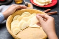 Woman putting apple slices into dish with raw dough at black table, closeup. Baking pie