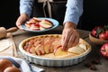 Woman putting apple slices into dish with raw dough at wooden table, closeup. Baking pie