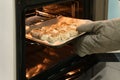 Woman putting baking tray with delicious cinnamon buns into oven