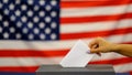 Woman putting a ballot in a ballot box on election day. Close up of hand with white votes paper on usa flag background. Royalty Free Stock Photo