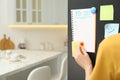 Woman putting blank to do list on refrigerator door in kitchen, closeup. Space for text Royalty Free Stock Photo