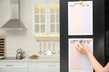 Woman putting blank to do list on refrigerator door in kitchen. Space for text Royalty Free Stock Photo