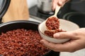 Woman putting brown rice into bowl from multi cooker in kitchen Royalty Free Stock Photo