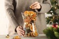 Woman putting Christmas tree ball into glass vase with dry orange slices and cones at white wooden table, closeup, Festive decor