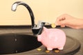 Woman putting coin into piggy bank near metal tap. Water saving concept Royalty Free Stock Photo