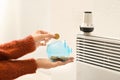 Woman putting coin into piggy bank near thermostat on calorifer. Heating saving concept Royalty Free Stock Photo