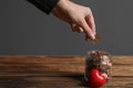 Woman putting coins into donation jar on wooden table against grey background, closeup. Royalty Free Stock Photo