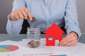 Woman putting coins into glass jar near model house. Royalty Free Stock Photo