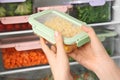 Woman putting container with corn in refrigerator with frozen vegetables