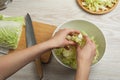 Woman putting cut Chinese cabbage into bowl at white wooden kitchen table, top view