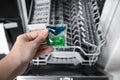 Woman putting detergent pod into open clean modern empty automatic dishwasher machine in kitchen, closeup