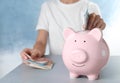 Woman putting Euro banknote into piggy bank at table, closeup. Money savings