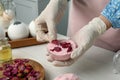 Woman putting flower petals in bath bomb mold at white table indoors, closeup Royalty Free Stock Photo