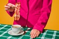 Woman putting fried bacon into cup with coffee over yellow background. Funny morning. Vintage, retro style interior