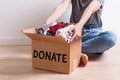 Woman putting her clothes in a carboad box with text Donate written on it.
