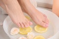 Woman putting her feet into bowl with water, roses and lemon slices on floor, closeup. Royalty Free Stock Photo