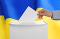 Woman putting her vote into ballot box against national flag of Ukraine, closeup