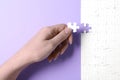 Woman putting last piece of white puzzle on violet background