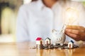 A woman putting light bulb over a piggy bank with house models and pile of coins on the table Royalty Free Stock Photo